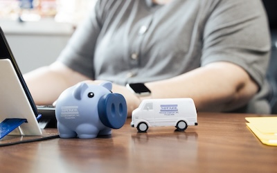 Person working on a laptop with a toy pig and toy work van in the foreground